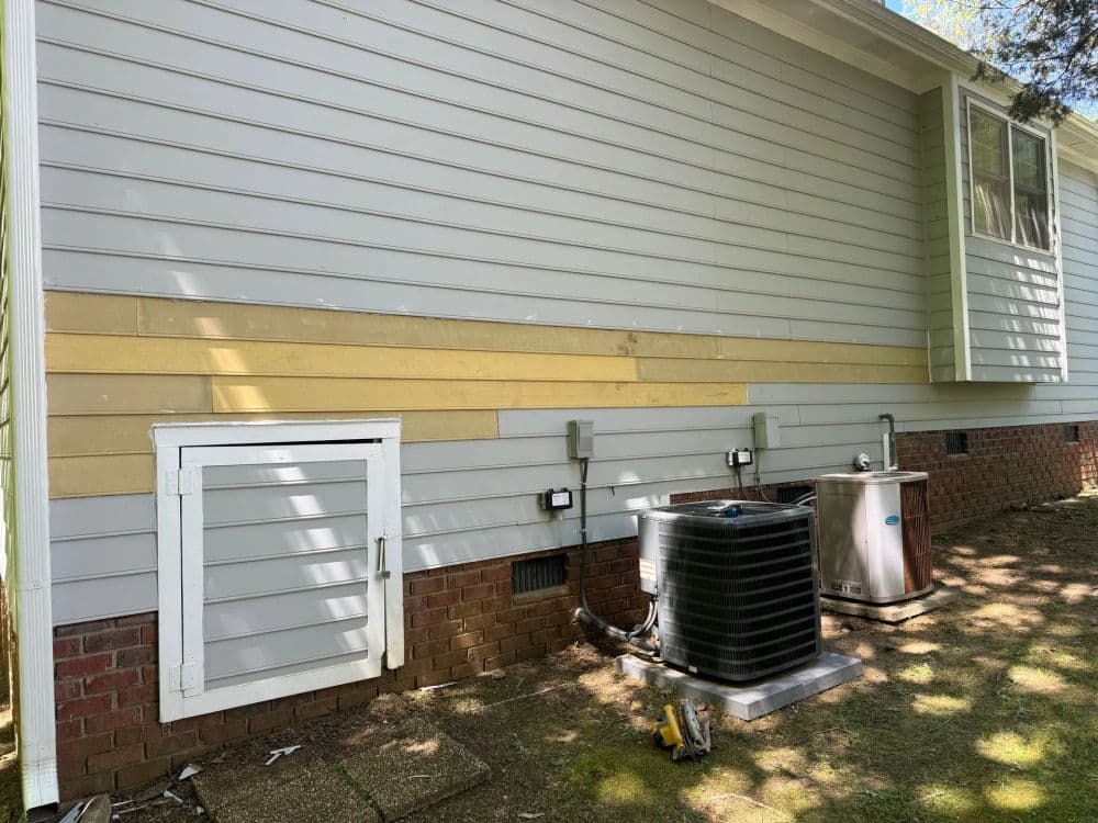 Side view of a house showing newly painted siding, air conditioning unit, and utility access door.