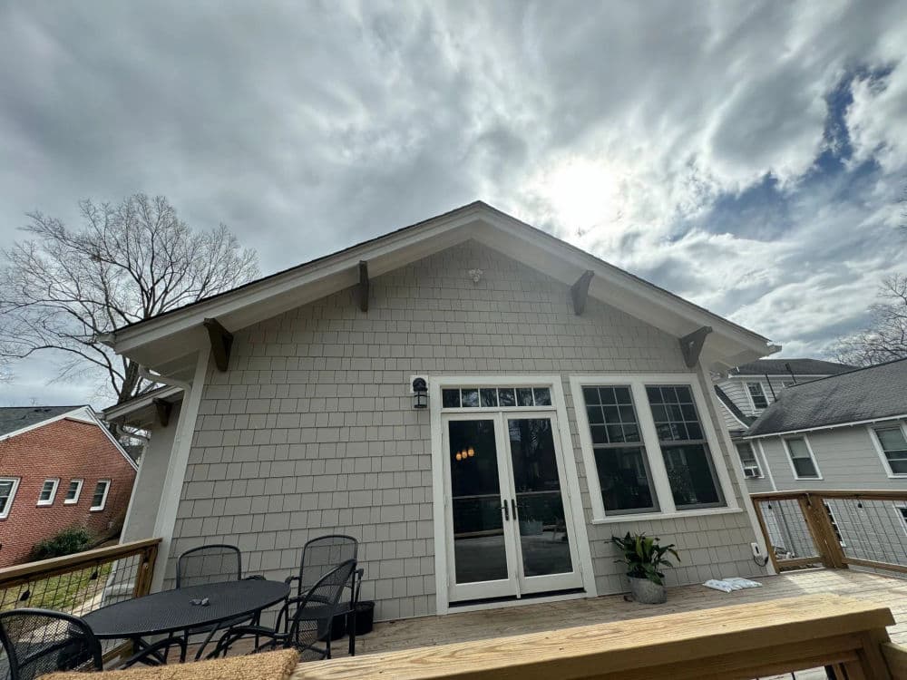 Modern house exterior with deck, large windows, and cloudy sky backdrop.