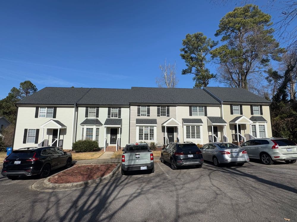 Row of townhouses in a residential area with parked cars and clear blue sky.