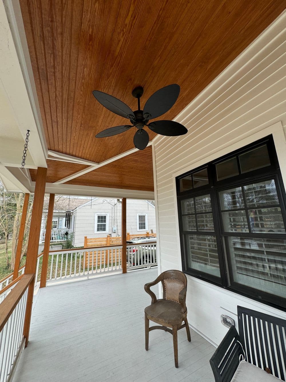 Ceiling fan on a porch with wooden ceiling, white railings, and a rustic chair.