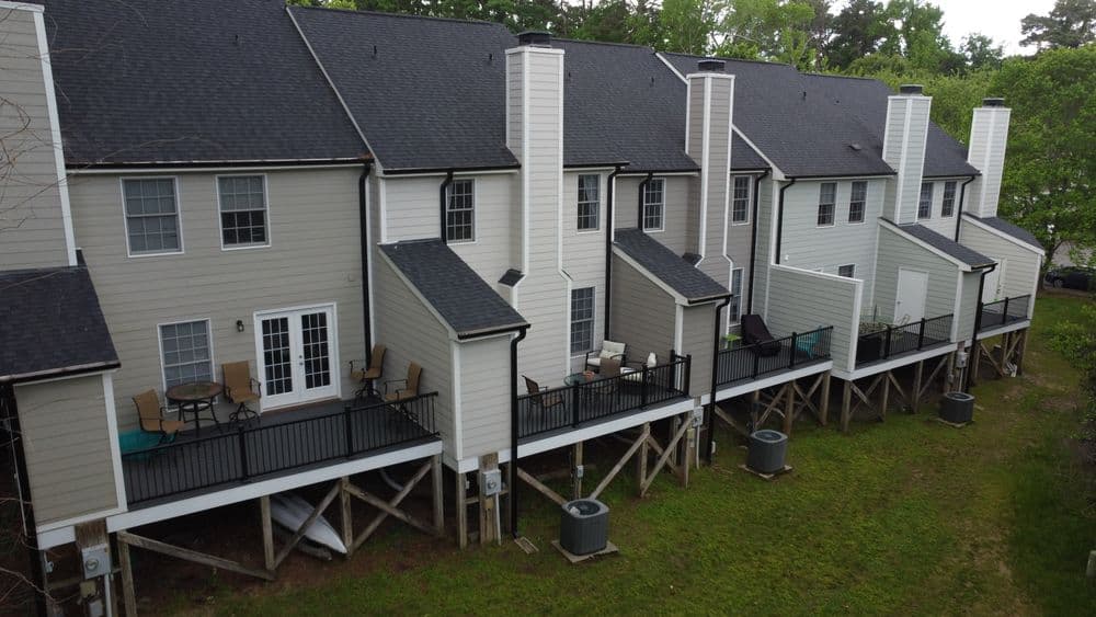 Row of modern townhouses with porches and air conditioning units in a green setting.