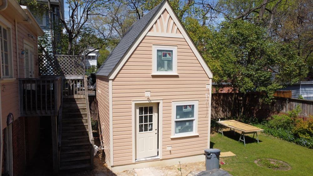 Exterior of a small, pink cottage-style house with a gable roof and green yard.