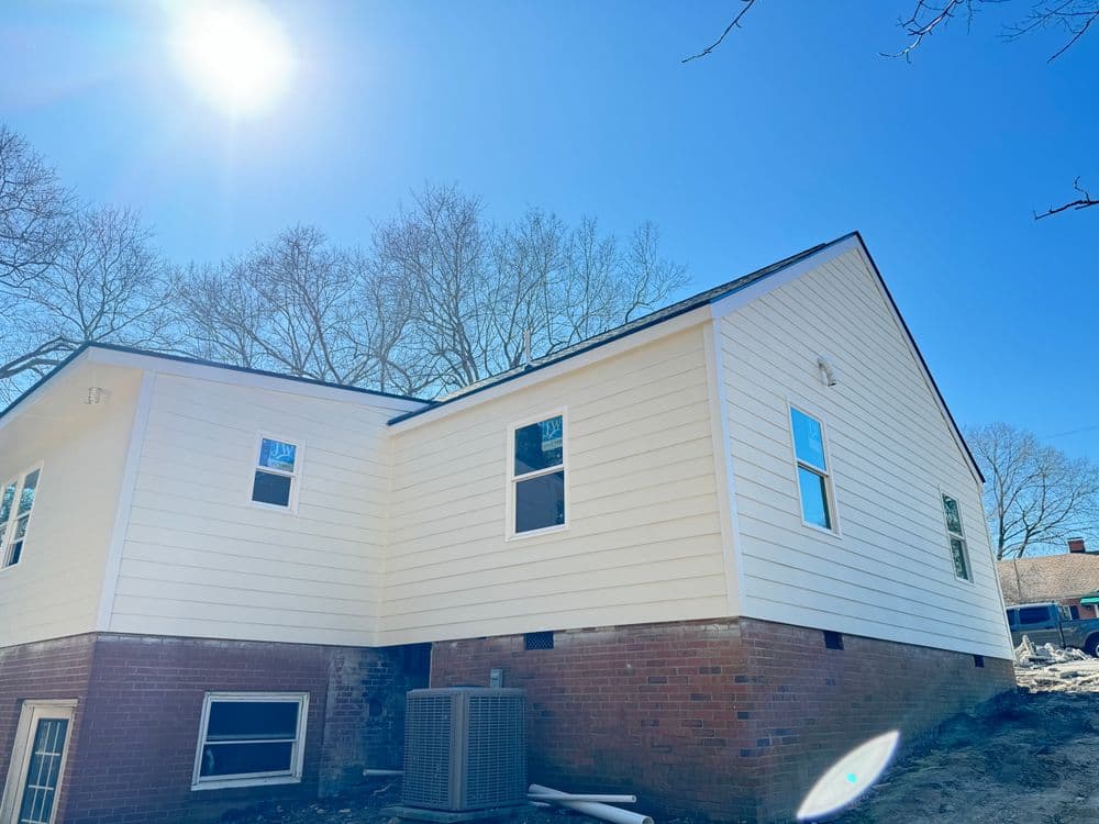 White house exterior with new siding, windows, and sunlight under a clear blue sky.