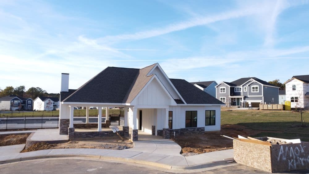 Newly constructed white house with stone accents, standing near modern residential buildings.