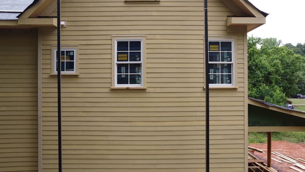 Newly constructed yellow house exterior with multiple windows and building materials nearby.