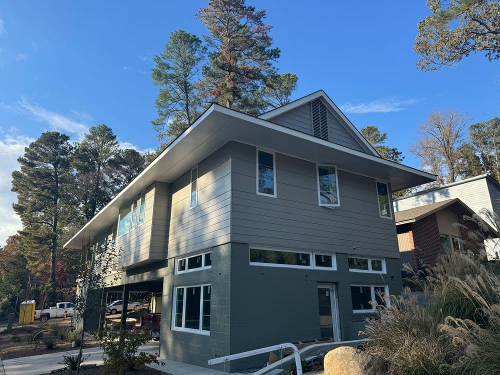 Modern two-story house with large windows, surrounded by trees and a clear blue sky.